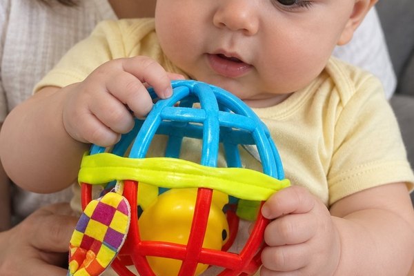 Bebé en brazos de su mamá toma la pelota de agarre metiendo los dedos por sus huecos